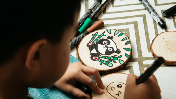 Close up of boy working on panda drawing on wood rounds